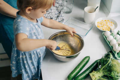Toddler daughter beats eggs with a whisk helping mom prepare an omelette.