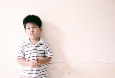 Portrait of cute boy standing by fish drawing on wall
