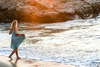 Girl in green dress seen from behind entering a beach at sunset 