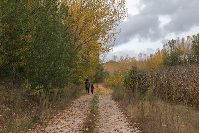 Rear view of woman with boy walking on footpath during autumn