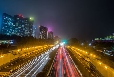 Light trails on road amidst buildings against sky at night