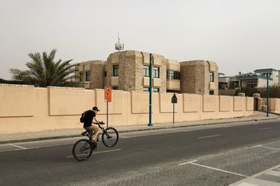 Man cycling on bicycle in city against clear sky