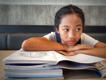 Girl with hand on chin looking away while studying at home
