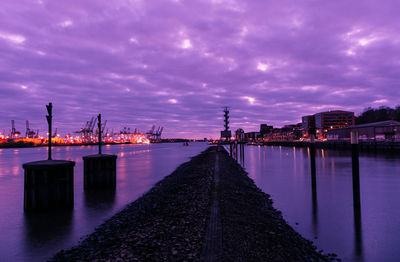 Illuminated bridge over river against sky at sunset