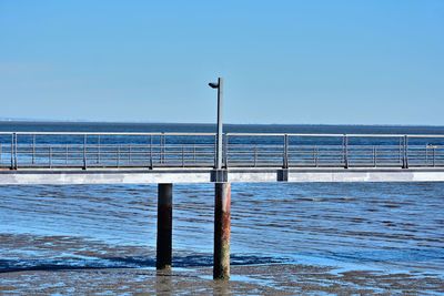 Pier over sea against clear blue sky