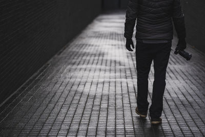 Low section of man walking on footpath with camera