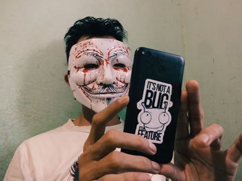 Close-up of young man with mask using mobile phone while standing against wall