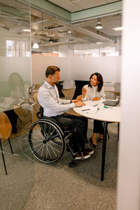 Smiling businesswoman discussing sales plans with disabled manager while sitting in board room