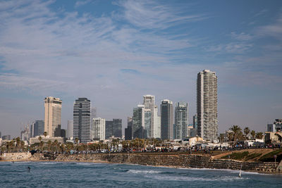 Sea by modern buildings against sky in city