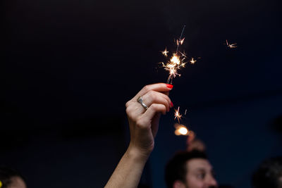 Cropped hand of woman holding lit sparkler at night
