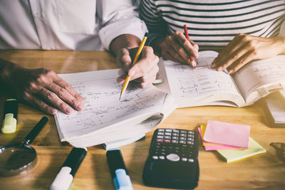 Midsection of business people working while sitting on table in office