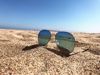 Surface level of sunglasses on beach against clear sky