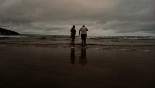 Rear view of friends standing on beach against sky