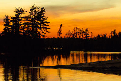 Silhouette trees by lake against sky during sunset