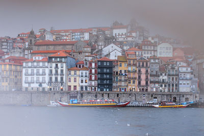 Boats in river by cityscape against sky