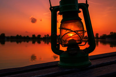 Close-up of illuminated lamp by lake against sky during sunset