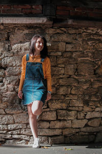 Full length of young woman leaning on stone wall