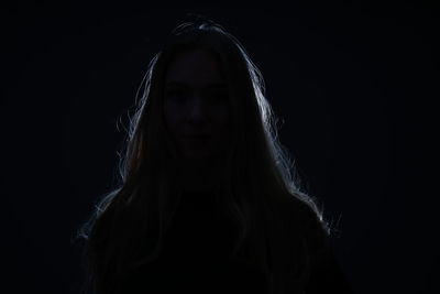 Portrait of young woman against black background
