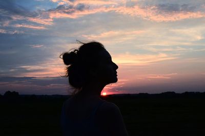Woman standing on silhouette field against sky during sunset