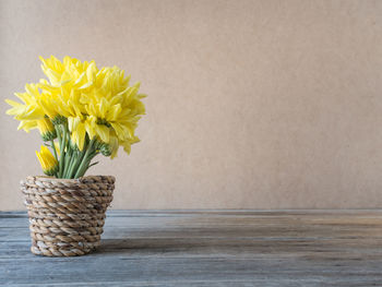 Close-up of yellow flower vase on table against wall