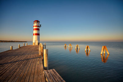 Lighthouse on pier over sea against clear sky