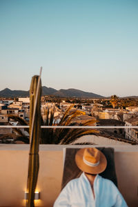 Anonymous traveler in robe with straw hat on face lying on sunbed while relaxing on rooftop against cloudless sunset sky during holidays in mallorca person