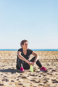 Full length of woman sitting on beach against sky