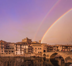 Rainbow over buildings in city against sky during sunset