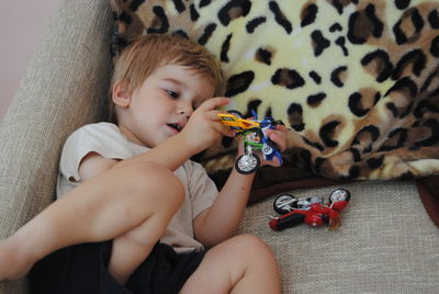 Cute boy playing with toy while lying on sofa at home