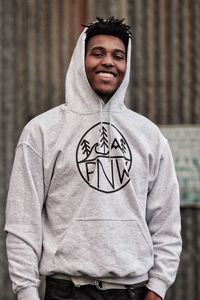 Portrait of smiling man wearing hooded shirt while standing outdoors