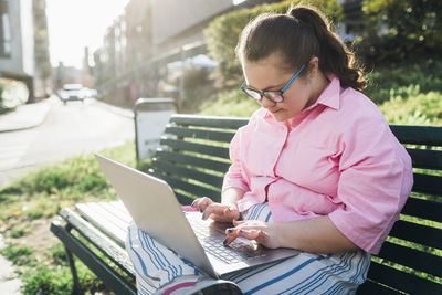 Teenage girl with down syndrome using laptop on bench in park