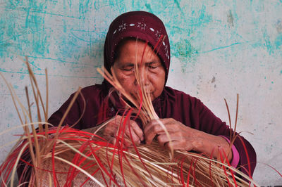 Portrait of a woman sitting against the wall making bamboo bags 