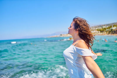 Side view of woman with arms outstretched standing against clear sky at beach