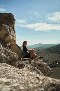 Side view of man sitting on rock against sky