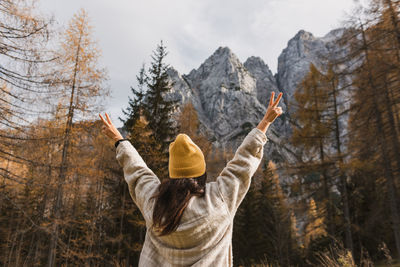 Rear view of young woman with raised arms standing under beautiful mountains in autumn