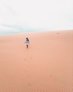 Woman walking on sand dune against sky