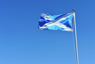 Low angle view of scottish flag waving against clear blue sky during sunny day