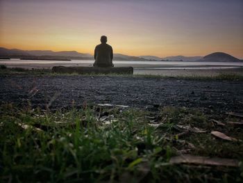 Rear view of man standing on field against sky during sunset