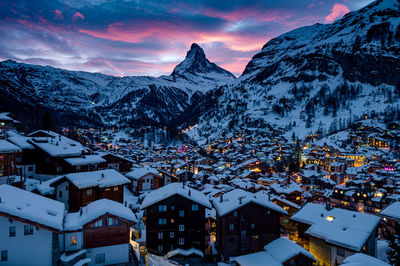 Snow covered houses and mountains against sky during winter