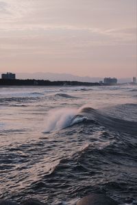 Waves rushing towards shore against sky during sunset