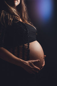 Close-up of pregnant woman touching her belly against black background