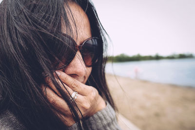 Close-up of woman with tousled hair wearing sunglasses against sky