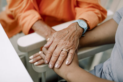 Midsection of female nurse and senior woman consoling while sitting with holding hands