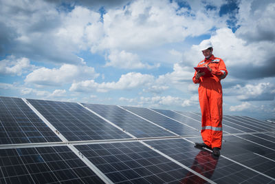 Engineer standing on solar panel against cloudy sky