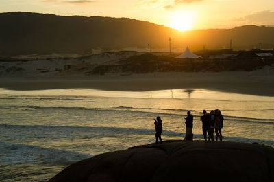 Silhouette people standing on shore by sea against sky during sunset