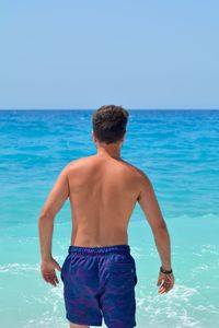 Rear view of shirtless man standing at sea against sky