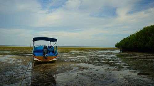 Boat moored on shore at beach against sky during low tide