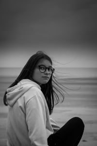 Portrait of girl sitting at beach against sky