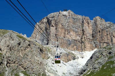 Low angle view of overhead cable car against rocky mountains during sunny day