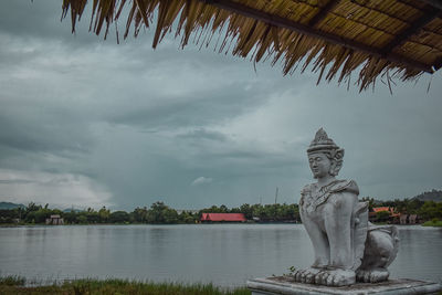 Statue by lake against sky